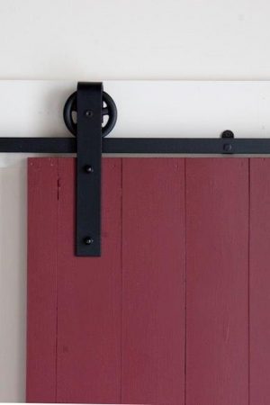 Photo of our large spoked flat track hardware mounted on a red barn door. Hardware kit manufactured by Better Barns, sold by Specialty Doors